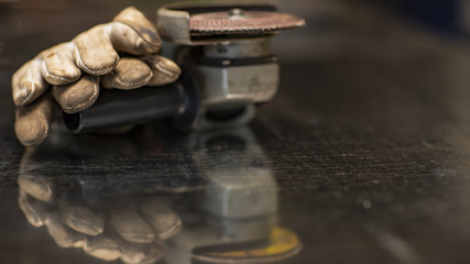 Manual electric sander, protective gloves, background blur and reflection on the table 