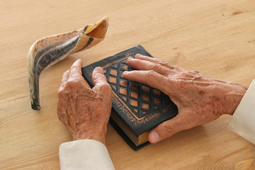 Old Jewish man hands holding a Prayer book, praying, next to shofar (horn). Jewish traditional...