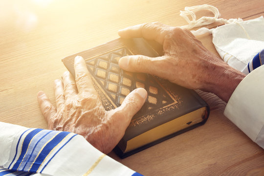 Old Jewish man hands holding a Prayer book, praying, next to tallit. Jewish traditional symbols. Rosh hashanah (jewish New Year holiday), Shabbat and Yom kippur concept.