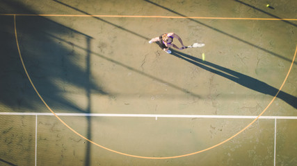Aerial image of a young woman playing tennis on a tennis court shot from overhead with a drone © Dewald