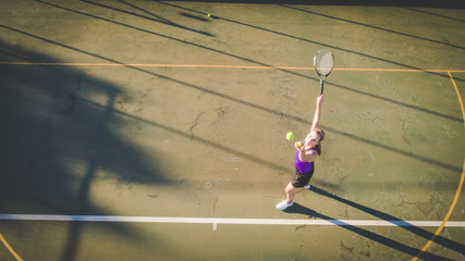Aerial image of a young woman playing tennis on a tennis court shot from overhead with a drone