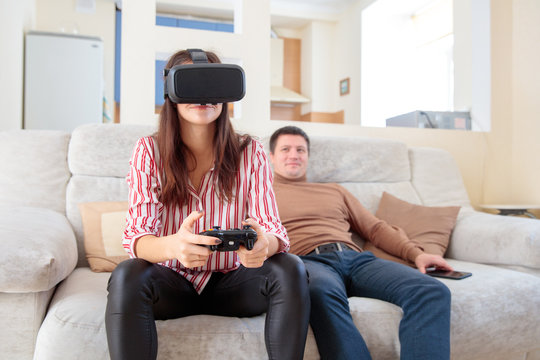 young woman  in virtual reality glasses with joystick and  young man on the couch