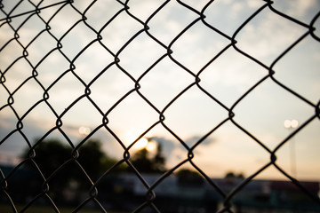 Fototapeta premium Sunrise sunset through chain link fence in bokeh background, wallpaper.
