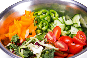 Fresh, healthy, organic ingredients for making vegetable salad. Tomatoes, cucumbers, green and yellow peppers, mixed green salad, sliced and placed in mixing bowl