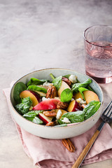 Bowl of salad with peaches, plums, spinach leaves, pecan nuts, honey and goat cheese on wooden cutting board. 