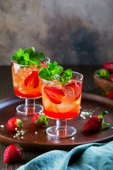 Red cocktail with ice, mint leaves and strawberry on wooden background.