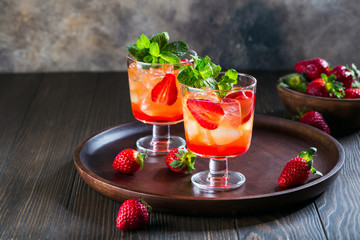 Red cocktail with ice, mint leaves and strawberry on wooden background.