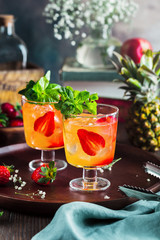 Red cocktail with ice, mint leaves and strawberry on wooden background.