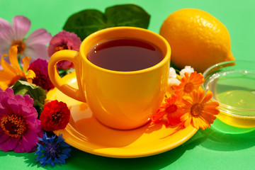 Tea with honey and lemon. A yellow cup of tea, honey, lemon and bright flowers create a spring and summer atmosphere. Breakfast in bright floral colors.