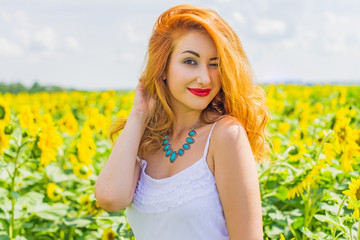 Naklejka na ściany i meble Candid red haired woman in white dress in the sunflowers at middle of a field in summer. Wellness concept, positive emotions and lifestyle. 