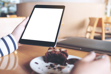 Mockup image of woman holding black tablet pc with blank white desktop screen while enjoy eating...