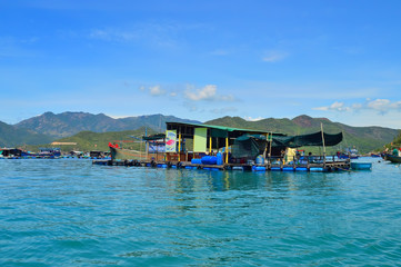 a floating fishing village in a sea bay, against a backdrop of mountains covered with tropical vegetation, clouds and a blue sky, Vietnam