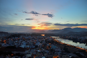 colorful equatorial sunset, against the backdrop of city buildings, mountains in the background, the setting sun and clouds, Vietnam