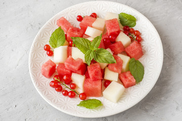 Salad of fresh juicy pieces of watermelon, melon, red currant and mint leaves on a plate.