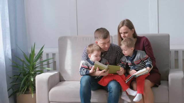 Family mom, dad and two twin brothers read books sitting on the sofa. Family reading time.
