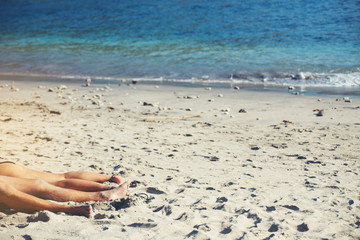 Fototapeta na wymiar The legs of couple relaxing on a sandy beach at the sea.