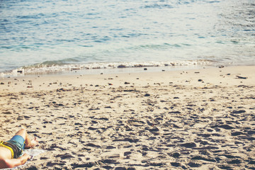 The legs of a man relaxing on a sandy beach at the sea.