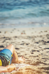 The legs of a man relaxing on a sandy beach at the sea.