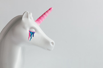 White painted unicorn head with colorful tears and pink horn on bright white background. Minimal...