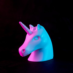 White painted unicorn head in bold pink and blue neon colors on dark background. Minimal art fantasy concept.
