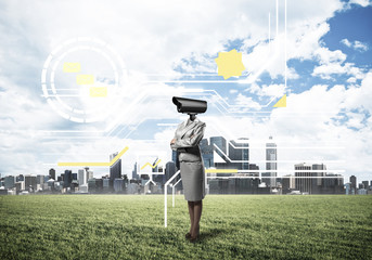 Camera headed woman standing on green grass against modern citys