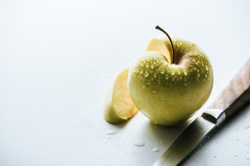 close up view of apple with cut piece and knife near by on white backdrop