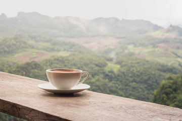 A cup of coffee on the table and a beautiful mountain background.