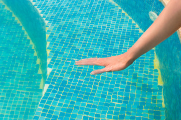 Young girl testing the swimming pool temperature with her hand in the water
