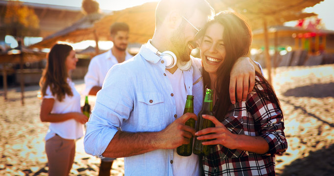 Happy couple smiling and drinking beer at beach