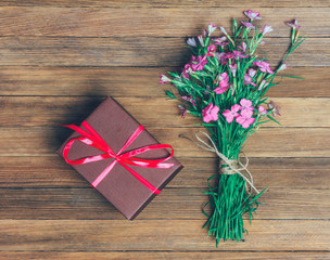 bouquet of carnations and brown box with a gift on a wooden background, flat lay top view