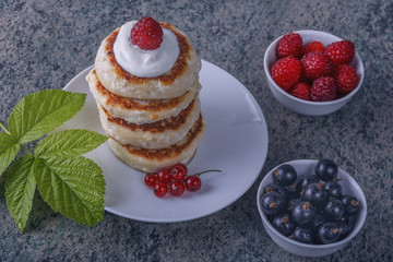 a pile of pancakes with cream and fresh berries on a wooden background