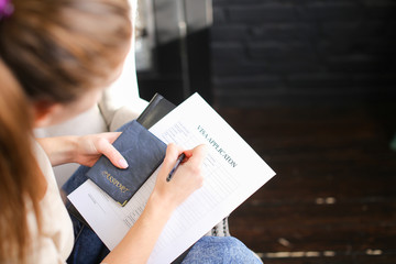 girl filling visa application form, student sitting on grey chair with passport. Young fair-haired...