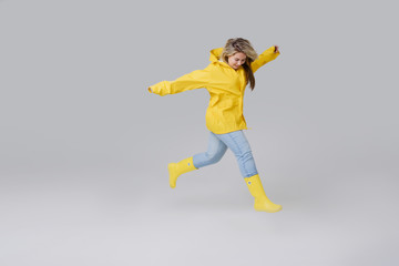 Young woman blonde in a yellow raincoat and yellow rubber knee-boots on a white background. Gladly steps after a rain and jumps over through puddles 