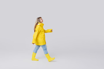 Fototapeta na wymiar Young woman blonde in a yellow raincoat and yellow rubber knee-boots on a white background. Gladly steps after a rain and jumps over through puddles 