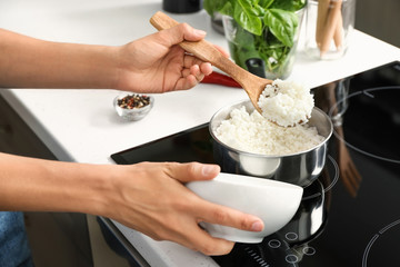 Obraz na płótnie Canvas Woman putting boiled rice into bowl in kitchen, closeup