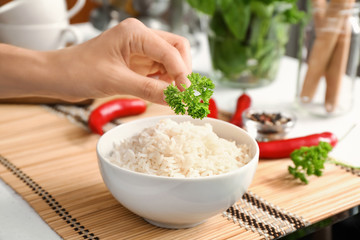 Woman putting parsley on boiled rice in bowl, closeup