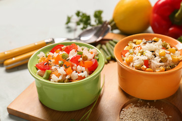 Bowls with tasty boiled rice and vegetables on wooden board