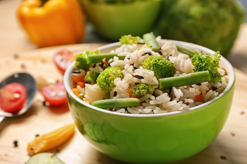 Bowl with tasty boiled rice and vegetables on table