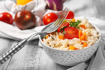 Bowl with tasty boiled rice and vegetables on wooden table