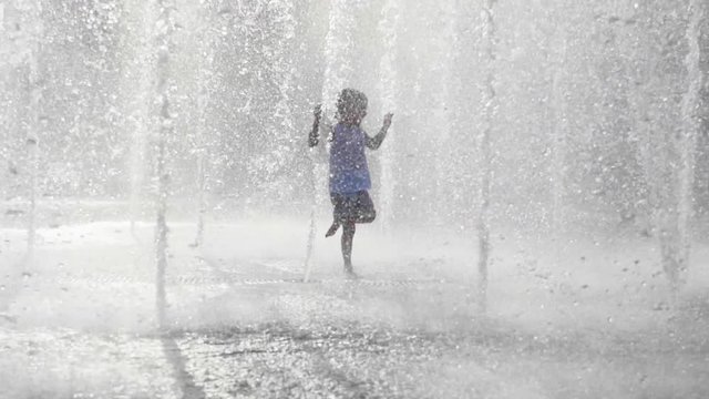 Wet little girl running and having fun in the jet fountain at city public park.
