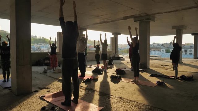 People yogis are standing with hands up in abandoned building in summer on sunset, healthy lifestyle, movement concept, sport concept