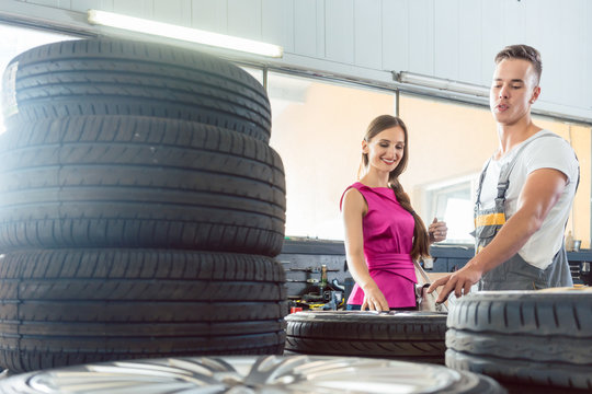 Handsome auto mechanic helping a female customer to choose from various high-quality tires in a contemporary automobile repair shop
