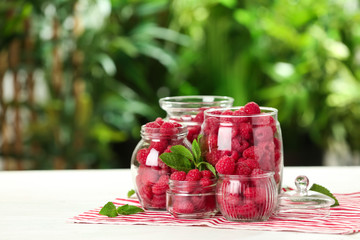 Glass jars with fresh ripe raspberries on table outdoors