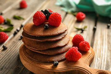 Tasty chocolate pancakes with berries on wooden table