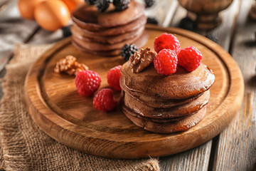 Tasty chocolate pancakes with berries on wooden board
