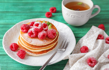 Plate with tasty homemade pancakes and cup of tea on wooden table