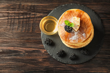Slate plate with tasty homemade pancakes, honey and blackberries on wooden table
