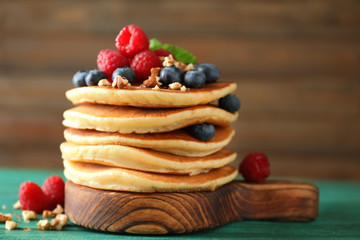 Tasty pancakes with berries and nuts on wooden board