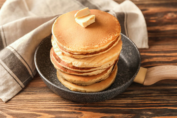 Frying pan with tasty pancakes on wooden table
