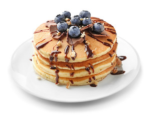 Tasty pancakes with chocolate sauce and blueberries on plate against white background